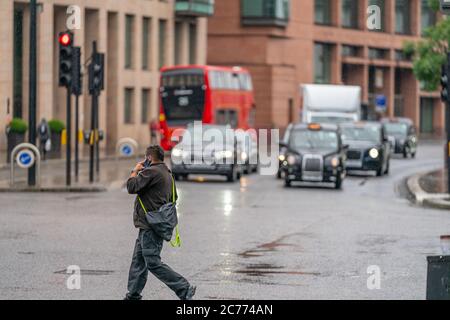 LONDON, ENGLAND - 10. JUNI 2020: Abgelenkter Mann, der die Straße überquert und an einem windigen Nieseltag in Holborn, London, mit seinem Mobiltelefon spricht Stockfoto