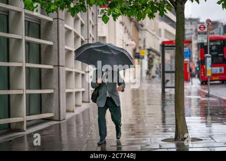 Ein Geschäftsmann mittleren Alters, der einen Anzug trägt, der während eines windigen, nieseligen Tages unter einem Regenschirm in Holborn, London durin, gegen den Wind kämpft Stockfoto