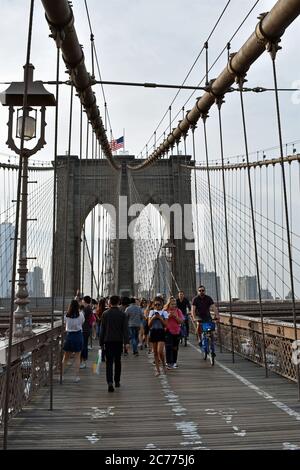 Menschen und Radfahrer überqueren die Brooklyn Bridge, New York City. Die Brückenkabel, die zum Stützturm führen, werden gesehen. Stockfoto