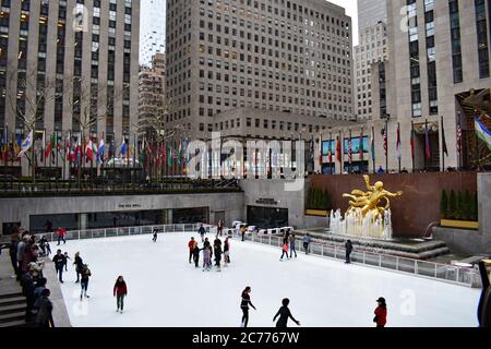 Eislaufen auf der Eisbahn im Rockefeller Center. Die goldene Prometheus Statue ist zu sehen, sowie Fahnen säumen den oberen Bereich um die Eisbahn. Stockfoto