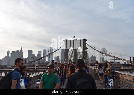 Besucher machen Selfies, bewundern die Aussicht und überqueren die Brooklyn Bridge in New York City. Hinter den Wolkenkratzern der Innenstadt sind die Wolkenkratzer zu sehen. Stockfoto