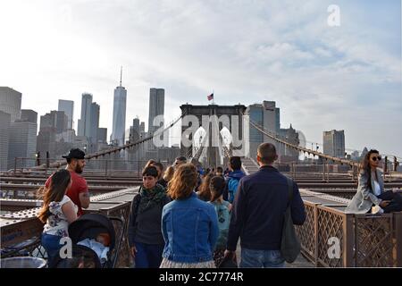 Besucher und Fußgänger überqueren die Brooklyn Bridge in New York City. Dahinter sind die Wolkenkratzer der Innenstadt zu sehen. One World Trade Center im Blick. Stockfoto