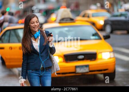 Junge Frau, die in New York City mit Telefon-App für Taxifahrt mit Kopfhörern pendelt von der Arbeit. Asiatische Mädchen glücklich SMS auf Smartphone Stockfoto