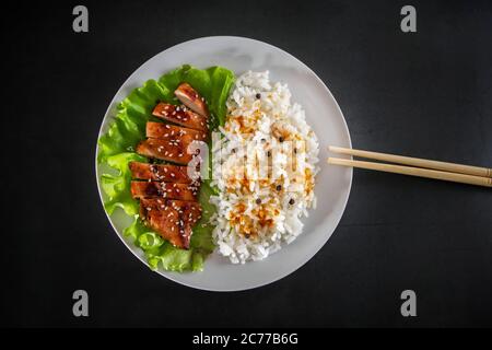 Teriyaki Huhn mit weißem Reis auf einem Teller. Leckeres Essen und chinesische Sticks auf dunklem Hintergrund Stockfoto