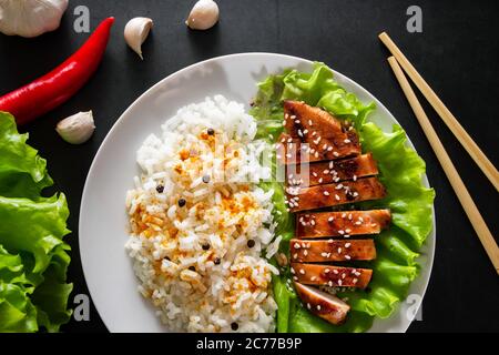 Teriyaki Huhn mit weißem Reis auf einem Teller. Leckeres Essen und chinesische Sticks auf dunklem Hintergrund Stockfoto