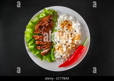 Hausgemachte Speisen - Teriyaki Huhn mit weißem Reis und Pfeffer auf schwarzem Hintergrund. Stockfoto