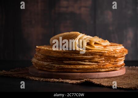 Ein Stapel dünner Pfannkuchen auf dunklem Holzhintergrund. Ein traditionelles Gericht von Crepes für den Urlaub Maslenitsa. Platz für Ihren Text, Foto für Design. Stockfoto