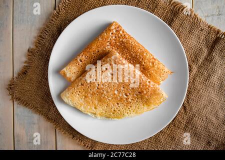 Pfannkuchen auf einem weißen Teller auf einem Leinenhintergrund. Russische traditionelle Lebensmittel Crepes für den Urlaub Maslenitsa. Flach liegend Stockfoto