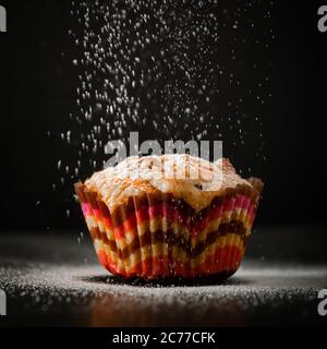 Leckere Muffins in Puderzucker auf schwarzem Hintergrund. Der Prozess der Herstellung von hausgemachten Kuchen. Stockfoto