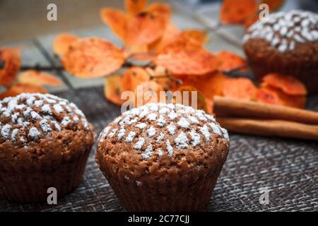 Schokoladen-Muffins mit Apfelfüllung auf einem Hintergrund aus Herbstblättern und Zimt Stockfoto