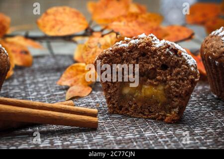 Schokoladen-Muffins mit Apfelfüllung auf einem Hintergrund aus Herbstblättern und Zimt Stockfoto