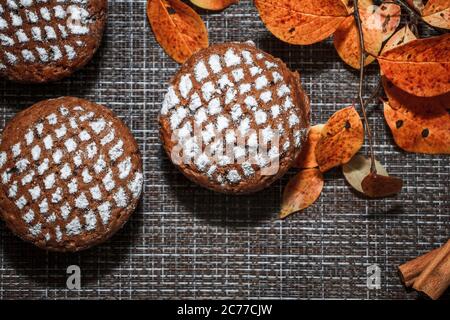 Schokoladen-Muffins mit Apfelfüllung auf einem Hintergrund aus Herbstblättern und Zimt Stockfoto