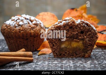 Schokoladen-Muffins mit Apfelfüllung auf einem Hintergrund aus Herbstblättern und Zimt Stockfoto