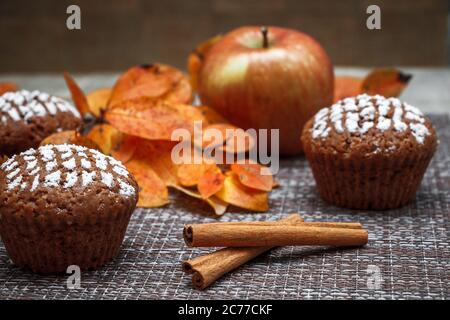 Schokoladen-Muffins mit Apfelfüllung auf einem Hintergrund aus Herbstblättern und Zimt Stockfoto