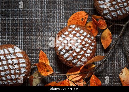 Schokoladen-Muffins mit Apfelfüllung auf einem Hintergrund aus Herbstblättern und Zimt Stockfoto