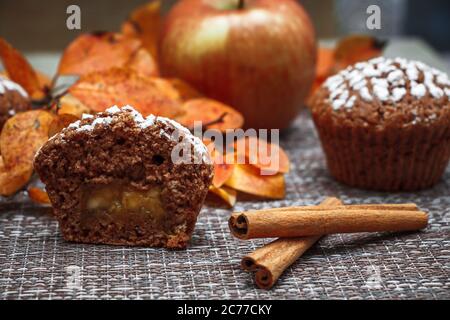 Schokoladen-Muffins mit Apfelfüllung auf einem Hintergrund aus Herbstblättern und Zimt Stockfoto