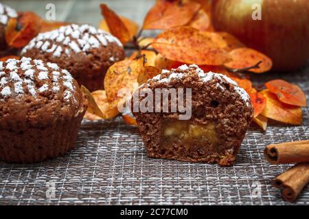 Schokoladen-Muffins mit Apfelfüllung auf einem Hintergrund aus Herbstblättern und Zimt Stockfoto