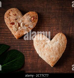 Herzförmige Kekse auf braunem Hintergrund. Zwei herzförmige Kekse mit Mandelnüssen auf Holzhintergrund. Symbol des Valentinstag Stockfoto