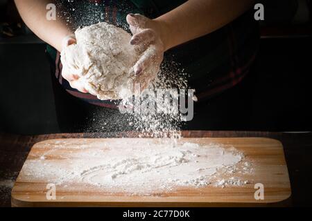 Die Hände des Kochs halten den Teig und machen Pizza. Mehl fliegt auf dunklem Grund Stockfoto