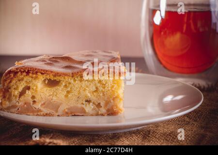 Hausgemachter Apfelkuchen auf einem Teller und Tee in einer transparenten Tasse auf braunem warmen Hintergrund Stockfoto