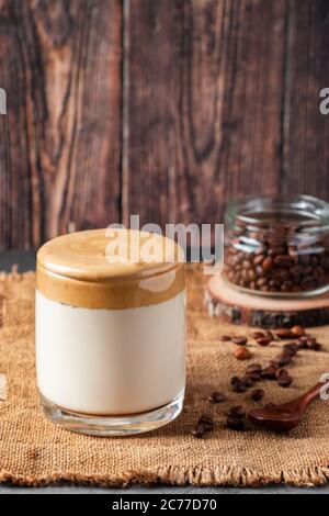 Dalgona Kaffee auf einem hölzernen Hintergrund. Ein Glas trendigen koreanischen Getränk aus Milch und süßem Schlagschaum. Rustikaler Stil, vertikales Foto Stockfoto