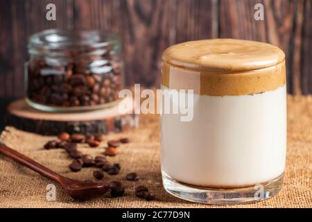 Dalgona Kaffee auf einem hölzernen Hintergrund. Ein Glas trendigen koreanischen Getränk aus Milch und süßem Schlagschaum. Rustikaler Stil Stockfoto