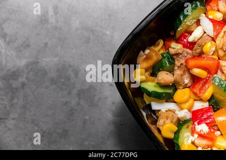 Heller Gemüsesalat mit Huhn auf grauem Betongrund. Machen Sie einen leckeren Salat für eine gesunde Ernährung. Nahaufnahme eines schwarzen Teils Stockfoto
