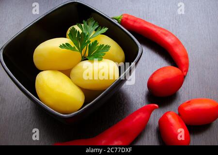 Gekochte Kartoffeln mit Chilischoten und Tomaten auf dunklem Hintergrund Stockfoto