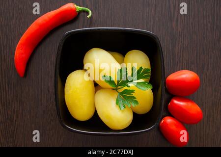 Gekochte Kartoffeln mit Chilischoten und Tomaten auf dunklem Hintergrund Stockfoto