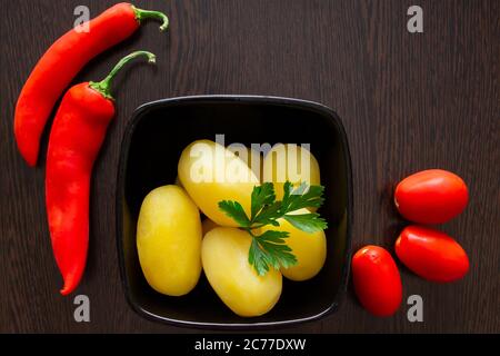 Gekochte Kartoffeln mit Chilischoten und Tomaten auf dunklem Hintergrund Stockfoto