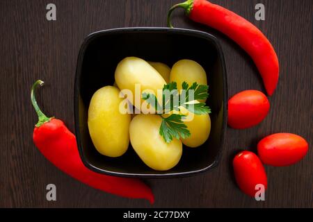 Gekochte Kartoffeln mit Chilischoten und Tomaten auf dunklem Hintergrund Stockfoto