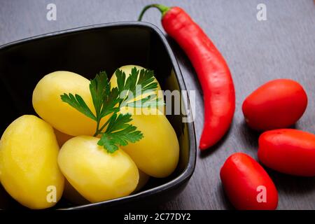 Gekochte Kartoffeln mit Chilischoten und Tomaten auf dunklem Hintergrund Stockfoto