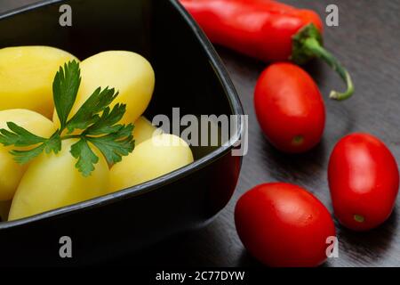 Gekochte Kartoffeln mit Chilischoten und Tomaten auf dunklem Hintergrund Stockfoto