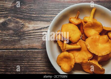 Frische Ernte der Pfifferlinge in einer weißen Schale auf einem hölzernen Hintergrund. Für Text platzieren. Stockfoto