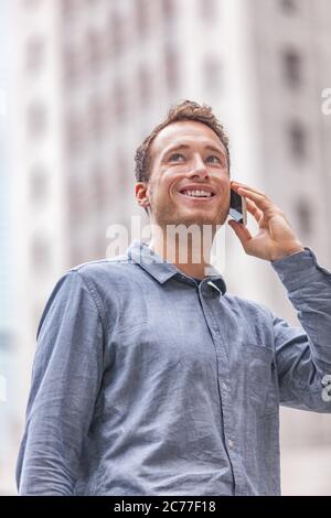 Junger städtischer Geschäftsmann, der in der Stadt auf der Straße telefoniert und am Handy spricht. Glücklich lächelnden Mann Porträt draußen mit Gebäude Stadtbild Hintergrund Stockfoto