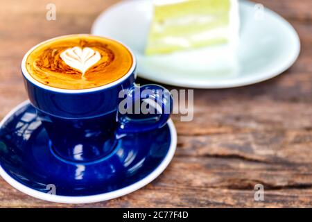 Nahaufnahme von heißem Cappuccino-Kaffee im Café, herzförmiger Cappuccino-Kaffee in blauer Tasse auf einem Holztisch mit Kopierfläche. Stockfoto