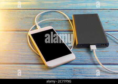 Smartphone-Ladefunktion mit Powerbank auf blauem Hintergrund und Kopierplatz. Smartphone-Ladefunktion mit Powerbank über weißes USB-Kabel. Stockfoto