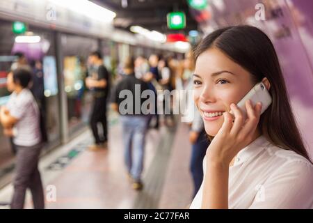 Geschäftsfrau in der U-Bahn-Station pendeln öffentlichen Verkehrsmitteln am Telefon sprechen, während zu Fuß zum ankommenden Zug. Asiatische Frau glücklich mit Handy Stockfoto
