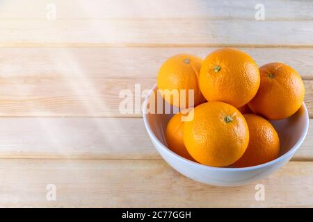 Frische Orangen in weißer Schale auf Holztisch. Stockfoto