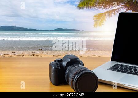 Digitalkamera und Laptop auf Holztisch mit Meer und Himmel Hintergrund. Mit Kopierplatz für Text oder Design. Stockfoto