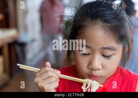 Asiatische Kind Mädchen mit rotem Kleid essen kleine Nudeln Suppe mit Essstäbchen Stockfoto