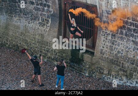 Fotografin und Assistentin, die eine Frau vor städtischem Hintergrund mit einer orangefarbenen Rauchbombe abschießen Stockfoto