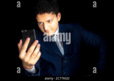 Portrait eines jungen Geschäftsmannes, der in seinem Geschäft Technologie verwendet, Aufnahme eines männlichen Geschäftsführers mit einem Smartphone und posiert in einem blauen Anzug isoliert Stockfoto