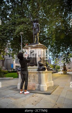 Jen Reid fotografiert ihre schwarze Kunstharz- und Stahlstatue mit dem Titel A Surge of Power (jen Reid) 2020 von Marc Quinn, wo sie auf dem leeren Edward Colston Sockel im Stadtzentrum von Bristol installiert wird. Stockfoto