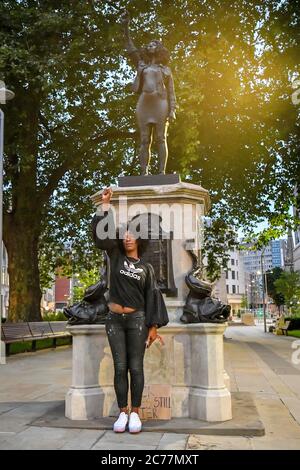 Jen Reid posiert vor ihrer schwarzen Harz- und Stahlstatue mit dem Titel A Surge of Power (jen Reid) 2020 von Marc Quinn, wo sie auf dem leeren Edward Colston Sockel im Stadtzentrum von Bristol installiert wird. Stockfoto