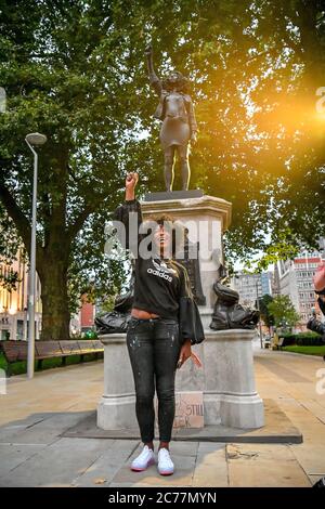 Jen Reid posiert vor ihrer schwarzen Harz- und Stahlstatue mit dem Titel A Surge of Power (jen Reid) 2020 von Marc Quinn, wo sie auf dem leeren Edward Colston Sockel im Stadtzentrum von Bristol installiert wird. Stockfoto