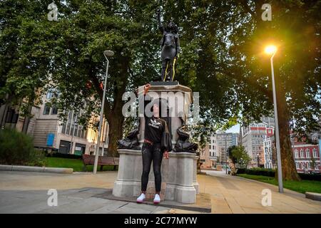 Jen Reid posiert vor ihrer schwarzen Harz- und Stahlstatue mit dem Titel A Surge of Power (jen Reid) 2020 von Marc Quinn, wo sie auf dem leeren Edward Colston Sockel im Stadtzentrum von Bristol installiert wird. Stockfoto