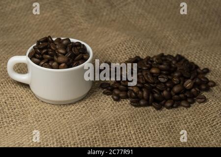 Frisch zubereiteter Kaffee in einer weißen Tasse, umgeben von Kaffeebohnen auf einem Holztisch. Frischer Kaffee. Stockfoto