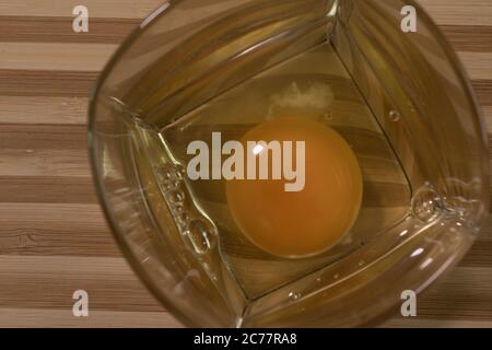 Rohes Ei in einem Glasbecher. Auf einem Holzbrett Stockfoto