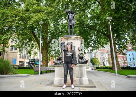 Jen Reid posiert vor ihrer schwarzen Harz- und Stahlstatue mit dem Titel A Surge of Power (jen Reid) 2020 von Marc Quinn, wo sie auf dem leeren Edward Colston Sockel im Stadtzentrum von Bristol installiert wird. Stockfoto